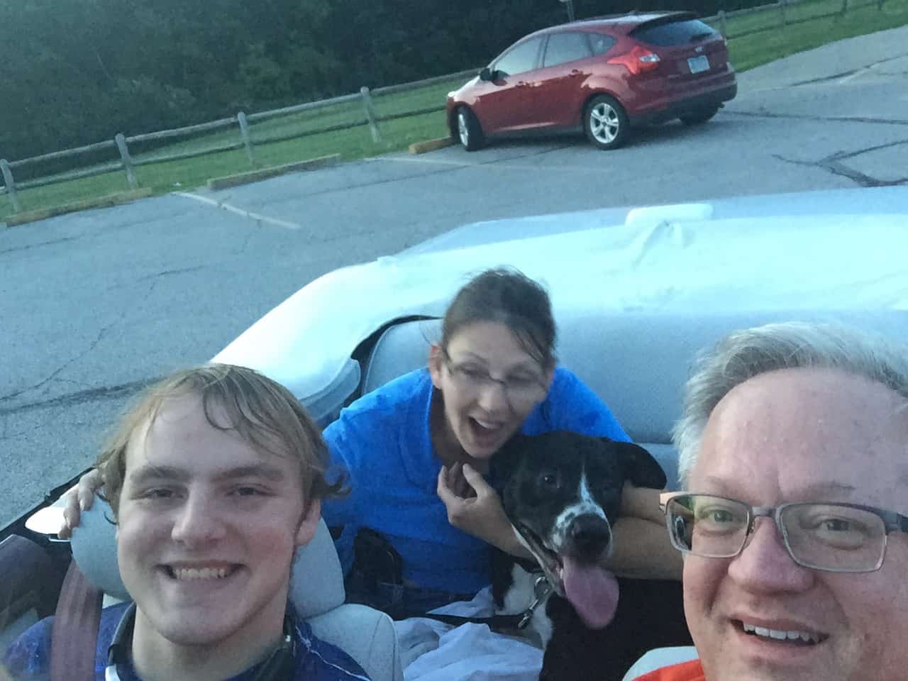 Man, boy, and woman sitting in a car and smiling. The woman is holding a puppy.