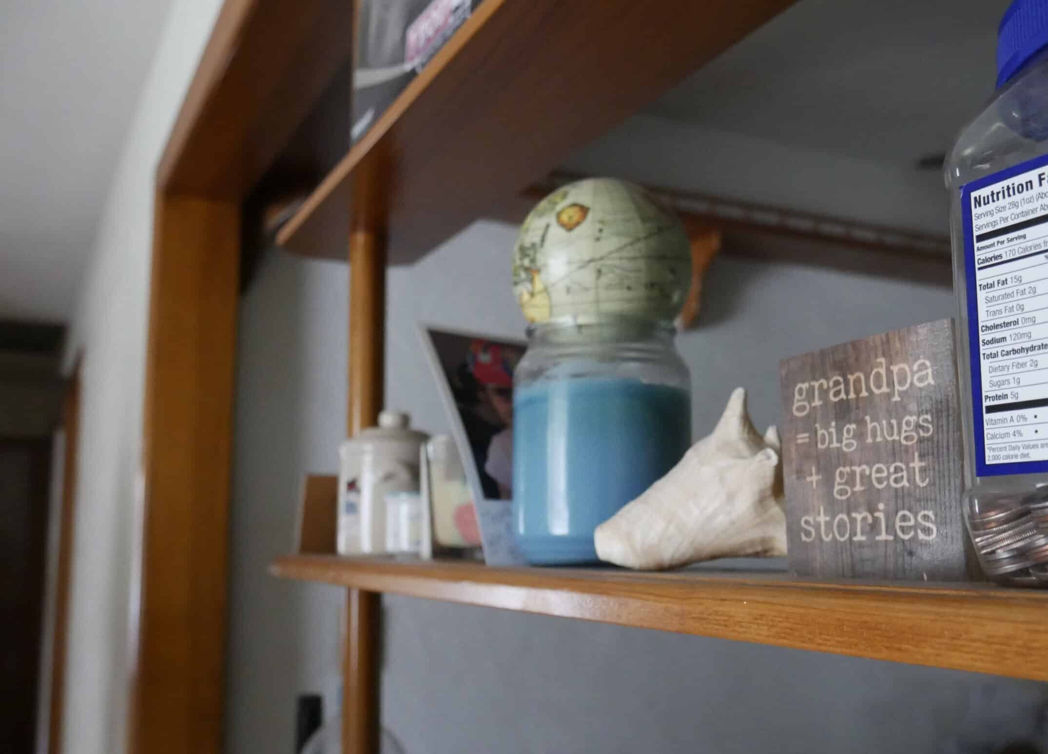 A collection of items on a shelf. One of the items is a globe, one is a seashell, and another is a sign that says "grandpa = big hugs and great stories"